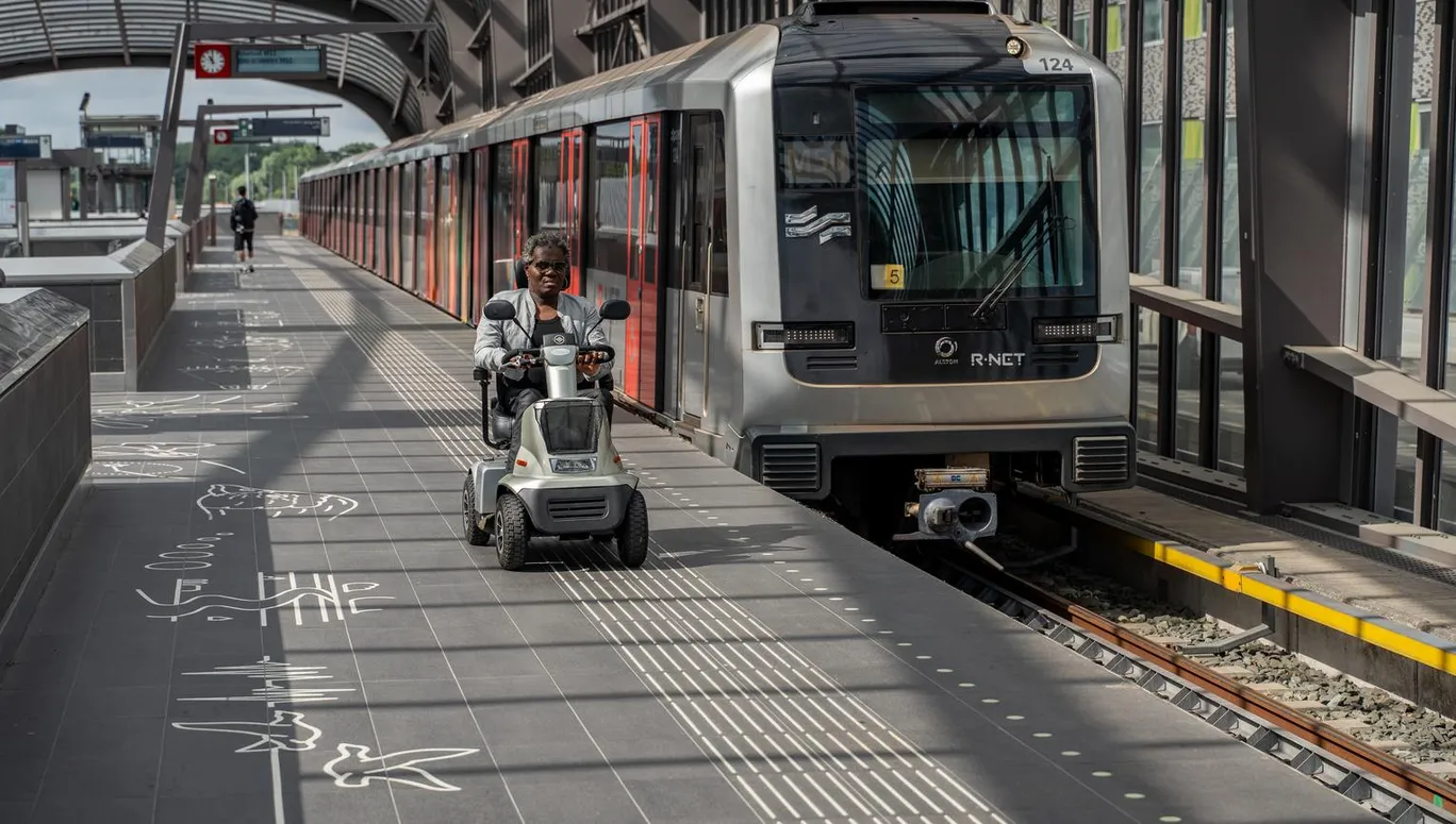 A person in an electric wheelchair riding on the metro platform.
