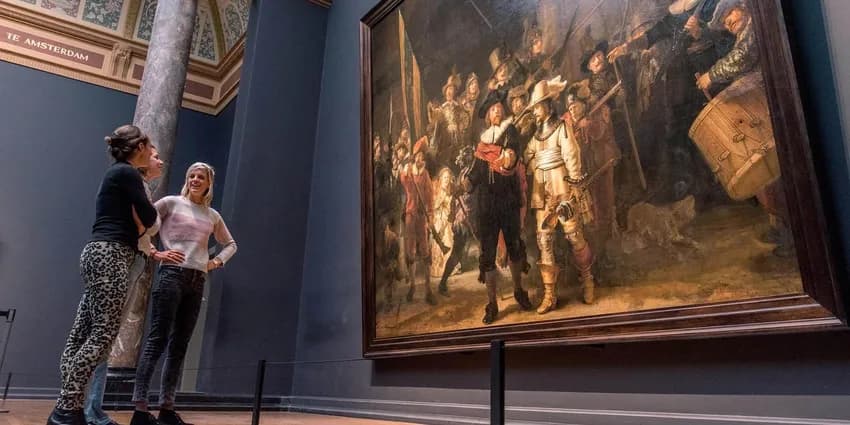 Three women gathered around Rembrandt's Nachtwacht (Nightwatch) painting in the Rijksmuseum.