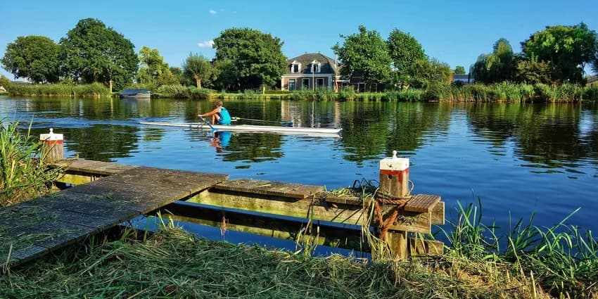 A woman in a rowboat rowing Amstelveen lake side